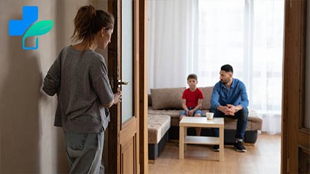 Женщина стоит за дверью и смотрит на мужа и сына, которые сидят на диване